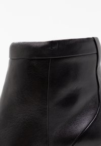 Stivaletto alla caviglia in pelle nera con texture liscia, bordo superiore arrotondato e dettagli di cuciture minime, che presenta un design elegante e moderno.