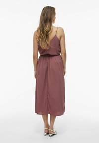 Mauve bezramenné maxi šaty s přiléhavým pasem, nařasením a splývavým lemem. Modelka má na sobě bílé sandály na podpatku.