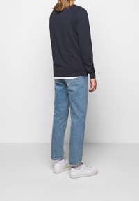 Sudadera azul marino con cuello redondo, combinada con vaqueros de corte relajado en azul claro y zapatillas blancas, vista desde atrás.