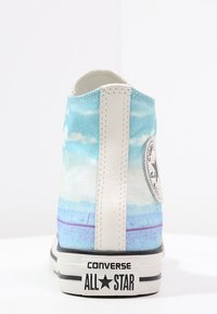 High-top tenisky Converse All Star s modrým vzorem oblohy a mraků, bílým pruhovaným podpatkem a značením na podrážce a boku.