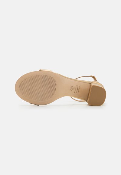 Sandal cu toc înalt bej, cu un design cu barete, talpă texturată și toc pătrat. Dispune de o cataramă mică pe brățara gleznei.