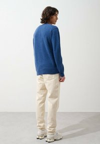 Pull en laine bleu avec un col rond, des poignets côtelés, associé à un jean écru et des baskets gris-blanc. La texture semble douce et tricotée.