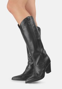 Botas de cuero negras hasta la rodilla con punta afilada, tacones gruesos y costuras decorativas a lo largo del cañón. Textura suave y diseño estructurado.