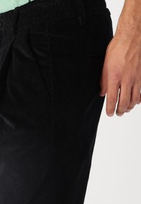 Svarte corduroy-bukser med strukturert ribbing, som har en løs passform og sidelommer. Livbåndet er elastisk for komfort.
