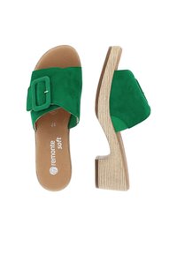 Sandali slide in suede verde con una fascia ampia caratterizzata da una fibbia rettangolare. Un tacco a zeppa con effetto legno offre altezza e stabilità.