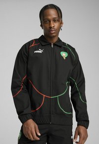 Sort atletisk jakke med lynlås, med flerfarvede buede linjer i rød og grøn. Logo på brystet og elastiske manchetter.