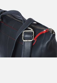 Marineblauwe leren handtas met een gestructureerd oppervlak, zilveren hardware, rode accenten en een rits sluiting. Voorzien van een verstelbare schouderband.