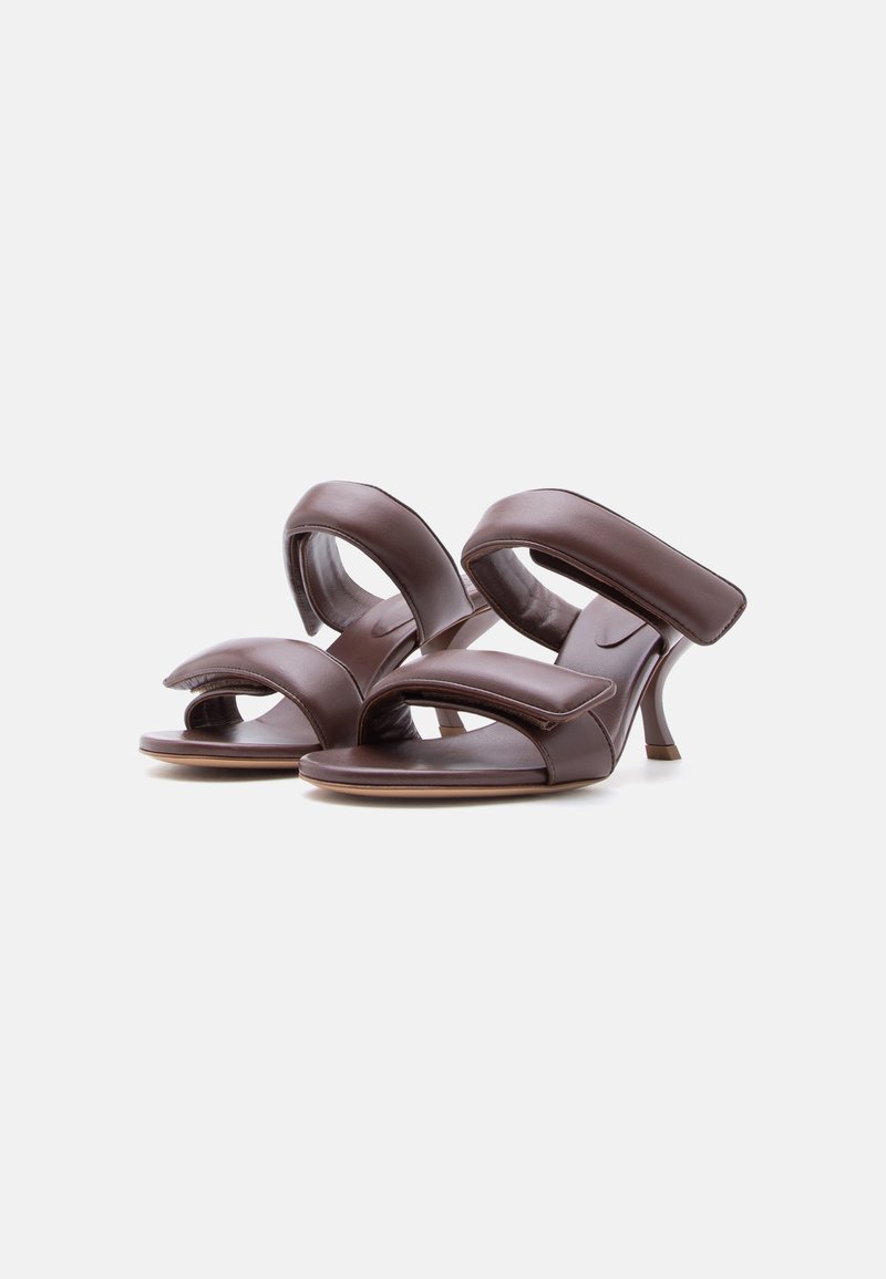 Een paar bruine open-toe sandalen met hoge hakken, twee gewatteerde banden en smalle stilettohakken op een witte achtergrond.