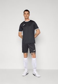 Donkergrijs sportshirt met witte accenten, gecombineerd met bijpassende shorts. Draag met witte sokken en voetbalschoenen, met een eenvoudig atletisch ontwerp.
