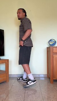 Calças de ganga escuras combinadas com uma camisa de manga curta xadrez. Ténis preto e branco com meias brancas até ao tornozelo. Piso interior suave.