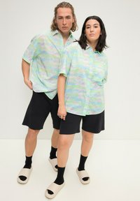 Kortærmede, knap-til skjorter i pastelgrøn med abstrakte mønstre, parret med sorte shorts og lyse slip-on sandaler.