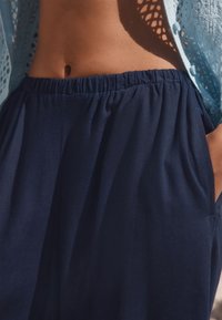 Navy blue, lightweight pants with an elastic waistband and side pockets. Worn with a light, crocheted, open-knit cardigan.