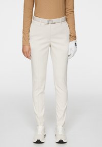 Białe spodnie golfowe o dopasowanym kroju, wykonane z gładkiego materiału. Szary pasek z prostokątną klamrą oraz białe sneakersy.