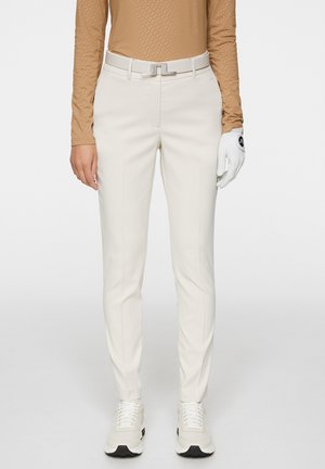 Witte golfbroek met een op maat gemaakte pasvorm, gemaakt van soepel stof. Een grijze riem met een rechthoekige gesp, gecombineerd met witte sneakers.