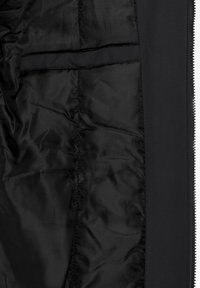 Intérieur de veste noire avec doublure lisse, couture verticale visible, fermeture éclair ouverte sur le côté droit, et une poche intérieure près du haut à gauche.