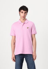 Rosa Poloshirt aus Baumwolle mit einem gelben gestickten Logo auf der linken Brust. Kurze Ärmel, flacher Kragen und gerader Schnitt.