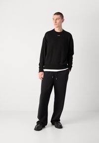 Schwarzer Rundhals-Sweatshirt mit kleinem Logo, kombiniert mit locker sitzenden schwarzen Jogginghosen und schwarzen Schuhen. Glatte Textur, lässiges Design.