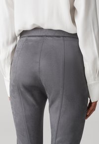 Graue Stretch-Hosen aus weichem, strukturiertem Stoff. Sie verfügen über einen glatten Bund und vertikale Nahtdetails entlang der Beine.