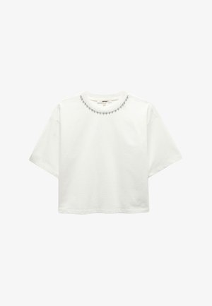 Camiseta blanca corta de algodón, con un escote redondeado adornado con pequeñas cuentas decorativas en el cuello. Mangas cortas.