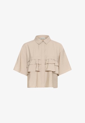 Beige kortärmad skjorta med knäppning fram, som har två horisontella volanger över bröstet och en mjuk, slät textur.