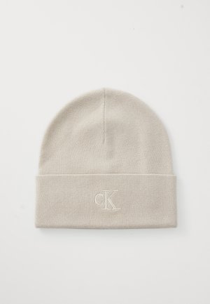 Light beige knit beanie with a folded cuff, featuring an embroidered "CK" logo in matching thread. Soft texture and snug fit.