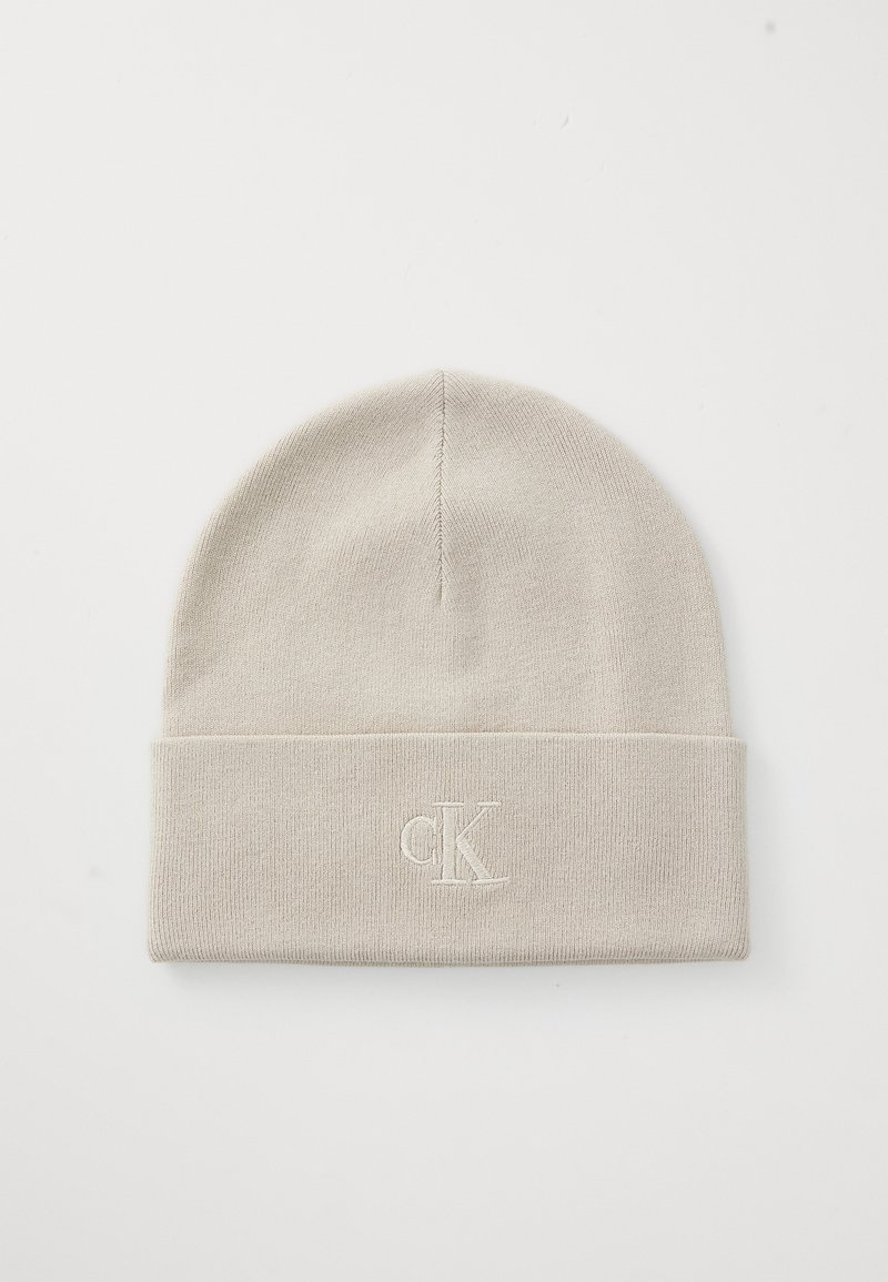 Light beige knit beanie with a folded cuff, featuring an embroidered "CK" logo in matching thread. Soft texture and snug fit.