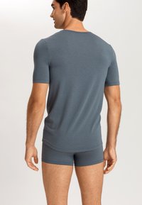 Grå kortärmad skjorta i mjukt material, matchat med tajta shorts. Bakifrån visas en avslappnad passform och slät textur.