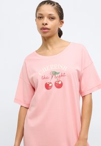 Ροζ βαμβακερό μπλουζάκι με κοντά μανίκια που διαθέτει γραφική εκτύπωση κερασιών και το κείμενο "CHERRISH the Night" σε ελαφρώς καμπυλωτό σχέδιο.