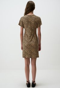 Tijgerprint jurk in beige en zwart, korte mouwen, aansluitende taille, knie lengte, gladde textuur, gecombineerd met zwarte sandalen.