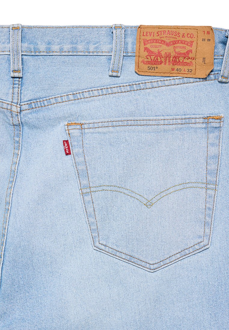 Jean en denim bleu clair avec une étiquette en cuir portant la mention "Levi Strauss & Co." au niveau de la taille, dotés d'un onglet rouge et de coutures jaunes.