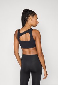 Μαύρο αθλητικό σουτιέν με σχεδιασμό κοψίματος στην πλάτη, κατασκευασμένο από λείο υλικό. Συνδυασμένο με μαύρο κολάν ψηλόμεσο, και τα δύο εφαρμοστά.