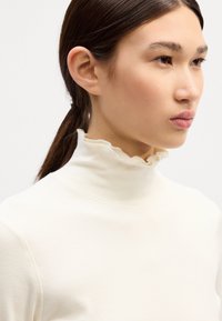 Cremefarvet turtleneck top lavet af ribbet stof, med en flæset krave, tætsiddende design og minimal sømsdetaljering.