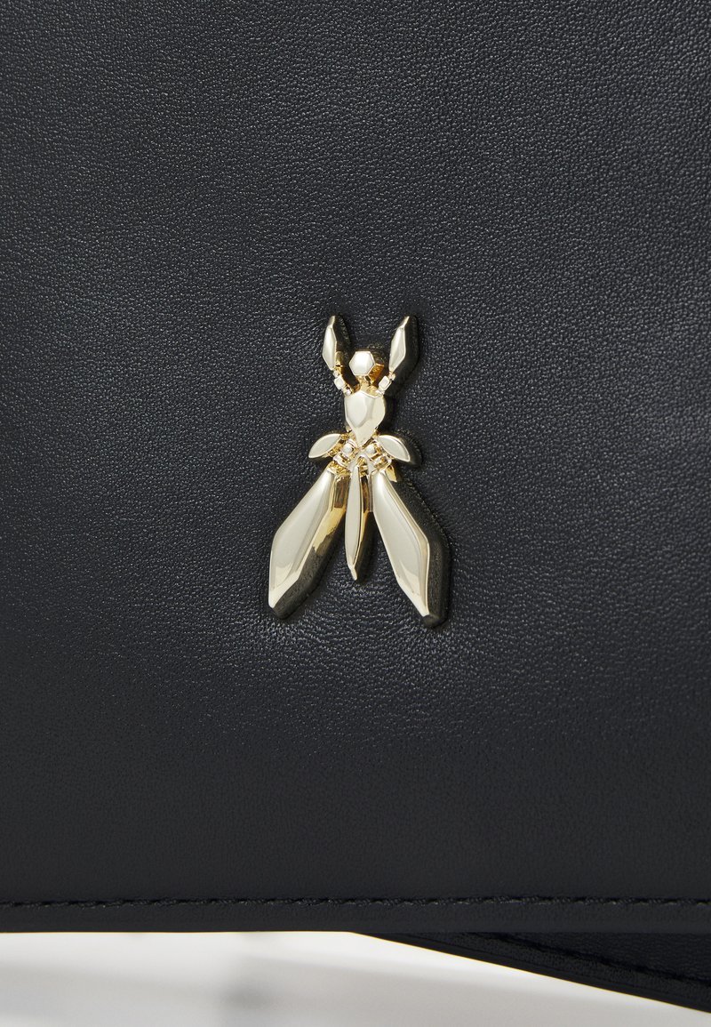 Un materiale nero testurizzato presenta un emblema di insetto dorato con dettagli angolari e riflettenti. Il design mette in risalto un'accentuazione unica e accattivante.