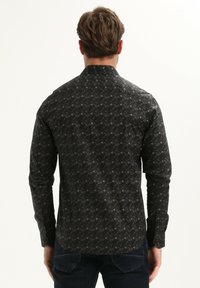 Camisa de manga larga en tejido negro con un patrón geométrico. Corte ajustado con cuello extendido y puños abotonados. Textura suave.