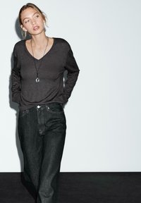 Tmavě šedý dlouhý rukáv v-neck top spárovaný s tmavými džíny. Košile má jemnou texturu, zatímco džíny mají klasický střih a decentní švy.