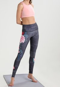 Vaaleanpunainen urheilutoppi yhdistettynä mustiin legginsseihin, joissa on pinkkejä ja turkooseja kukkakuoseja. Kankaan pintastruktuurissa on hienoja pisteitä ja raitoja.