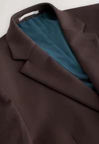 Bruine blazer met een gladde textuur, voorzien van een teal-gepatroneerde voering. Opmerkelijke details zijn onder andere een notch-kraag en een borstzak.
