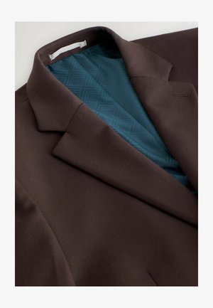 Brun kavaj med en slät yta, med ett foder med teal-mönster. Anmärkningsvärda detaljer inkluderar en snedskuren krage och en bröstficka.