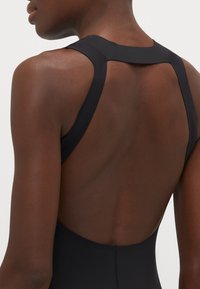 Maillot de bain noir avec un design à dos nageur, fabriqué en tissu lisse et extensible et doté d'un dos bas. Style minimaliste sans embellissements supplémentaires.