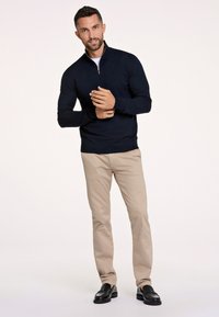 Maglione zip-neck blu navy, pantaloni beige e mocassini neri. Il maglione presenta una lavorazione a maglia testurizzata con polsini e orlo a coste.