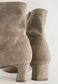 Brown suede ankle boots with a low block heel, featuring a zipper closure on the side and visible stitching details along the seams.