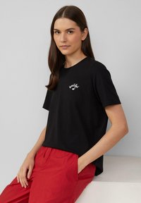 Zwarte katoenen T-shirt met korte mouwen, voorzien van een witte geborduurde tekst "beautiful". Gecombineerd met felrode broeken, gepresenteerd tegen een neutrale achtergrond.