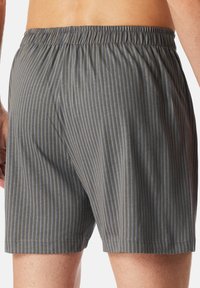 Harmaat uimapuvut, joissa on pystysuorat siniset raidat, joustava vyötärö ja sileä pinta. Ominaisuuksia ovat löysä istuvuus ja polven ylle ulottuva pituus.