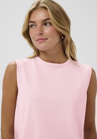 Rozā bezpiedurkņu topiņš, kas izgatavots no mīksta, teksturēta auduma ar apaļu kakla izgriezumu. Vienkāršs un minimālistisks dizains, piemērots ikdienas valkāšanai.