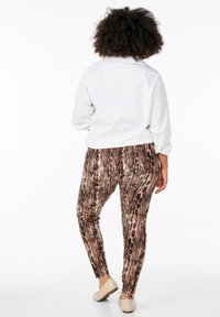 Aansluitende, gedessineerde legging in bruin en beige slangprint, gecombineerd met een witte blouse met knopen. Soepele textuur, taps toelopend ontwerp, eenvoudige schoenen.