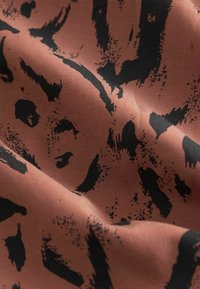 Textil i rostfärg med svart abstrakt tryck, med en mjuk yta, mjuk fall och subtil lyster.