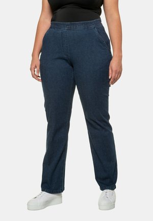 Pantaloni in denim blu scuro con vita elasticizzata, design a gamba dritta, tasche laterali e texture liscia; indossati con sneakers bianche.