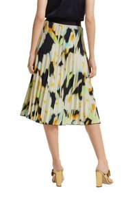 Falda plisada con una cinturilla negra, que presenta un patrón abstracto colorido en amarillo, verde y azul sobre un fondo claro.