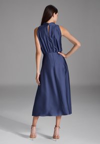 Robe en satin marine avec un col haut, une taille cintrée et un dos à découpe en forme de trou de serrure ; une silhouette évasée fluide.