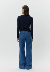 Topp med lange ermer i marineblått, kombinert med høytsittende, utsvingte blå jeans med et rent design og to baklommer. Myk tekstur generelt.